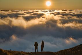 Silhouettes of the people, on the beautiful mountain, among the clouds, at colorful sunset in Clermont Ferrand, France