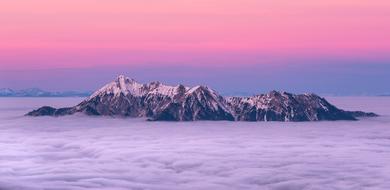 purple clouds on top of a mountain against a pink sunset