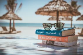 Colorful and beautiful books and sunglasses on the wooden surface in sunlight, on the sandy beach