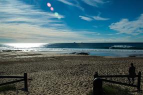 person sits on fence on Sand Beach in front of sea