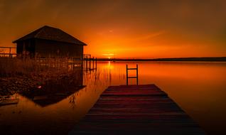 fishing house and wooden pier on an orange sunset background