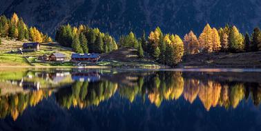 panoramic photo of the mirror lake, cottages and autumn trees at the foot of the Schladminger Tauern mountain range, Austria