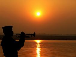 Trumpeter on riverside at sunset