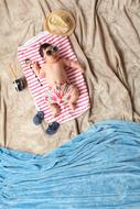 Cute baby with sunglasses resting on the red and white towel on the beach decorations