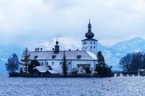 Beautiful, white castle among the snowy landscape with green trees in Gmunden, Austria