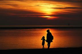 silhouette of mom and daughter on the seashore against the background of golden sunset