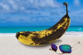 Banana with sunburn skin on the sandy beach with glasses lying near