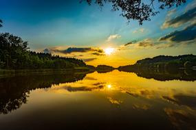 Beautiful lake, among the shore with trees, at colorful sunset on background