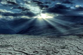 sunbeams through clouds over cracked ground in desert