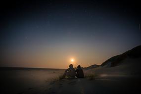 couple is sitting on the beach at sunset