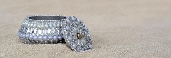 Beautiful, silver jewelry box with beads, on the sand