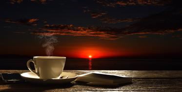 a cup of tea and a book on the table against a sunset background