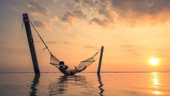 Person on a hammock above the water on beautiful waterscape at colorful sunset on Bali, Indonesia