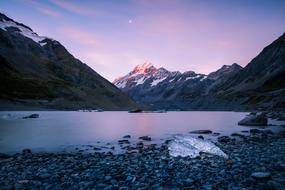 Beautiful, rocky seashore near the snowy mountains, at colorful sunset, in New Zealand