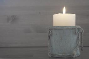 Close-up of the white, burning candle in the wooden cup