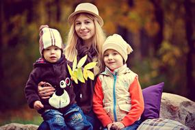 Blonde mother, with the children, in hats, with the colorful leaves, among the beautiful and colorful park, in the autumn