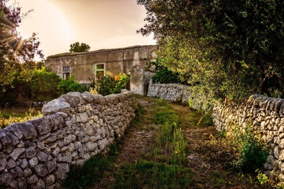 Beautiful driveway with the stone fence, among the colorful plants, in Sicily, Italy, at colorful and beautiful sunset