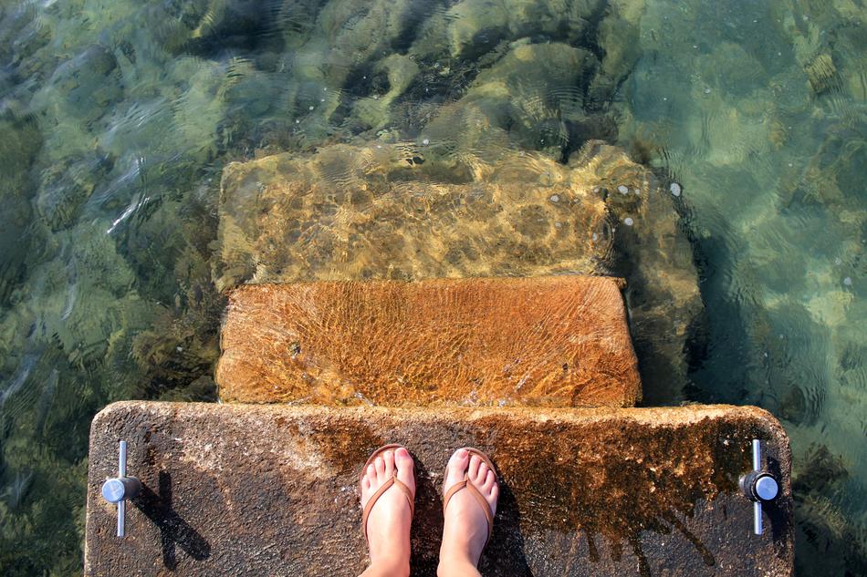 feet in flip flops on the steps in sea water