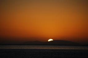 distant view of the setting sun over the mountains to the sea