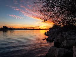 Beautiful landscape of the shore, with the rocks and trees, at beautiful and colorful sunset, among the clouds, in the evening