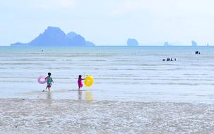 KIds, with the colorful toys, on the beach of Krabi, in Thailand, at background with the mountains