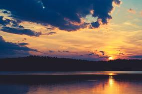 Beautiful landscape with the silhouettes of the hills, with the plants, behind the lake, at beautiful and colorful sunset