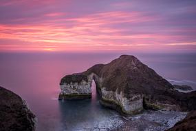 large rock in the sea against a pink sky