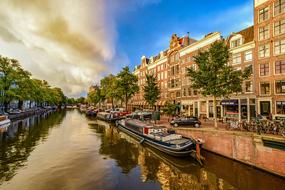 Beautiful landscape with the boats on the canal, among the buildings and green trees in Amsterdam, Netherland