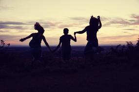 Silhouettes of the friends jumping on the beautiful landscape at colorful sunset
