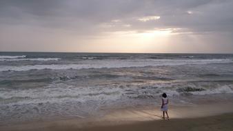Person, on the beautiful, sandy beach of the ocean, with the waves, at beautiful sunset