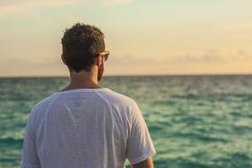 Back view of a man in glasses looking on the beautiful green and blue sea