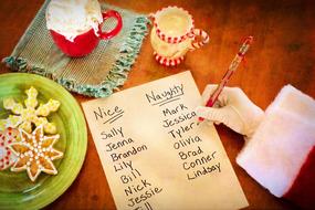 Person, writing in the Santa's list, near the colorful and beautiful drinks and cookies