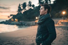 Profile portrait of a man in leather jacket, watching colorful and beautiful sunset, from the sandy beach