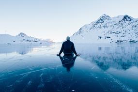 a lonely man sits on the ice of a frozen mountain lake
