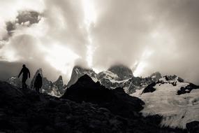 Black and white photo with the people on the beautiful, snowy mountains at cloudy sky on background