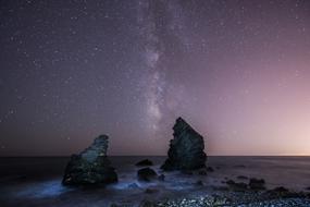 milky way in pink sky above sea boulders