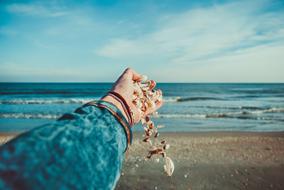 Beautiful and colorful necklace with seashells in the hand, on the beautiful sandy beach