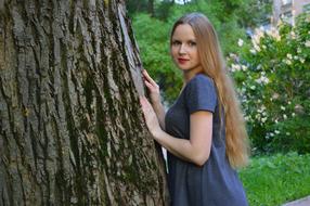 Smiling girl, near the tree, among the beautiful and colorful plants, near the buildings