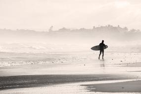 Silhouette of a surfer on the beautiful, foggy, sandy beach