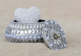 Beautiful, shiny jewelry box with beads, with the white, decorated heart inside, on the sand