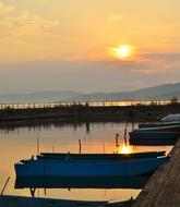 setting sun over the boats near the pier on the lake