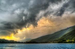 Beautiful landscape with the mountains under colorful sunrise in the grey clouds