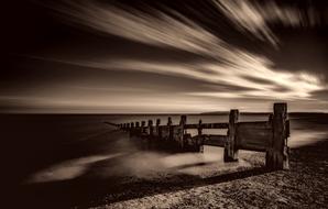 black and white photo of a pier at dusk on the sea