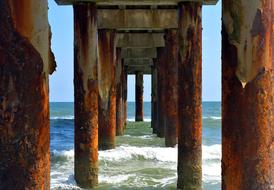 ocean waves under a rusty pier