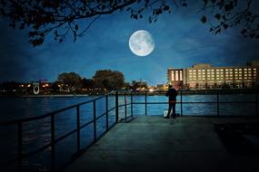 landscape of silhouette of a man standing on the embankment against the background of a very large moon