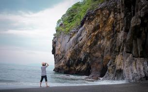Person on the beach, taking a photo of the beautiful and colorful cliff with the green plants