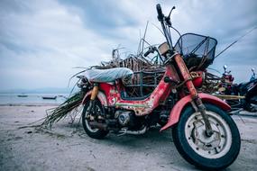 red dirty motorcycle is parked on the beach