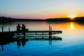 Silhouettes of the couple, in the beautiful dock, near the shore, at beautiful and colorful sunset