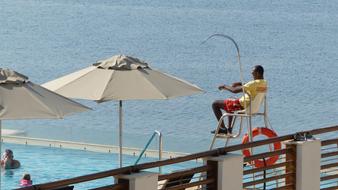 Lifeguard sitting, near the pool with the people, near the sea