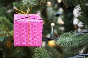 Beautiful pink Christmas gift and other decorations on the Christmas tree with green needles